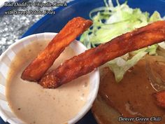 a blue plate topped with a sandwich covered in sauce and fried chicken strips next to a side salad