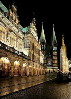 an old european city street at night with lights on and clock tower in the background