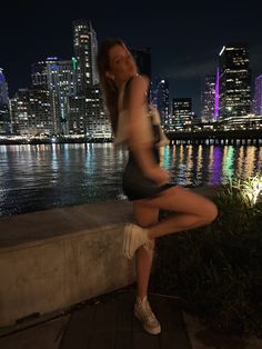 a woman is posing for a photo in front of the water at night with her legs spread out