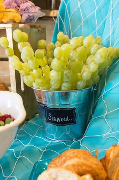 grapes and croissants sit in buckets on a table with blue cloth