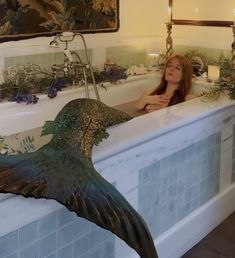 a woman sitting in a bathtub with a mermaid tail hanging from the tub and flowers on the wall