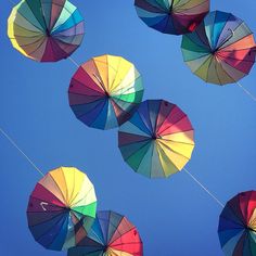 several multicolored umbrellas are flying in the air together on a sunny day