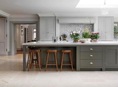 a large kitchen with two stools in front of the counter and an island that has potted plants on it