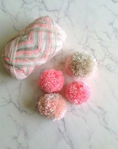 pink and white pom - poms sitting on a marble surface next to a ball of yarn