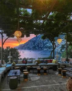 an outdoor seating area overlooking the ocean at sunset with hanging lights and lanterns above it