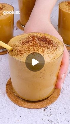 a person holding a cup filled with liquid on top of a table next to other cups