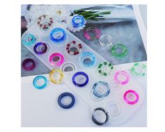 several different colored rings sitting next to each other on top of a white table with flowers in the background