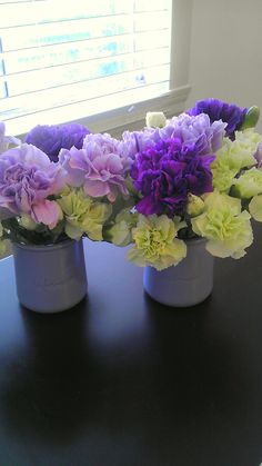 purple and white flowers are arranged in small vases on a table next to a window