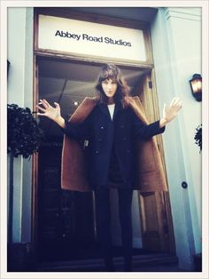 a woman standing in front of a doorway with her hands out to the side while wearing a coat