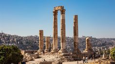 some people are walking around in front of some ancient ruins and trees with the city in the background