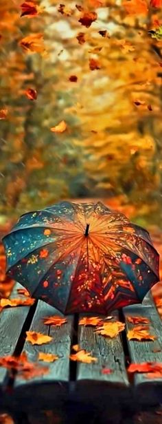 an open umbrella sitting on top of a wooden bench in the fall leaves near a body of water