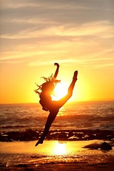 a woman doing a handstand in front of the sun on the beach at sunset