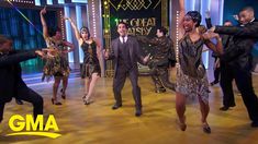 a group of people dancing on a stage with one man in a suit and the other woman in a dress