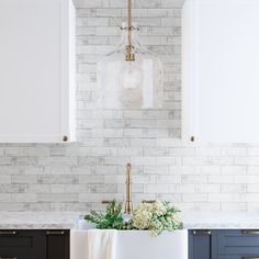 a kitchen with marble counter tops and white cabinets, hanging light fixture over the sink