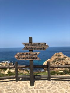 a wooden sign pointing in different directions on the side of a hill next to the ocean