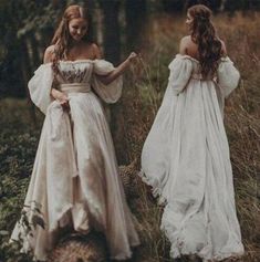 two women in white dresses walking through the woods