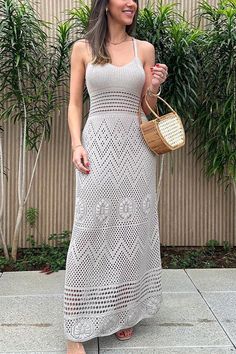 a woman in a white crochet dress is holding a straw bag and smiling