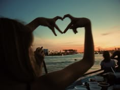 a woman holding up her hands in the shape of a heart at sunset on a boat