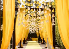 an outdoor ceremony with yellow draping and white flowers hanging from it's ceiling