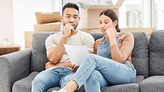 a man and woman sitting on a couch looking at paperwork