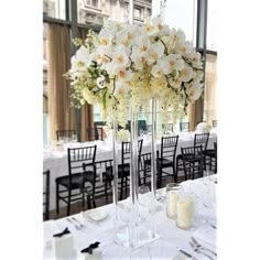 a tall vase filled with lots of white flowers on top of a table next to candles