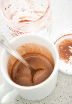 a cup of hot chocolate with a spoon in it next to a container of ice cream