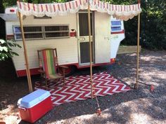 an old camper trailer is set up in the shade with chairs and coolers