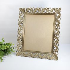 an ornate gold framed mirror sitting next to a potted plant on a white surface