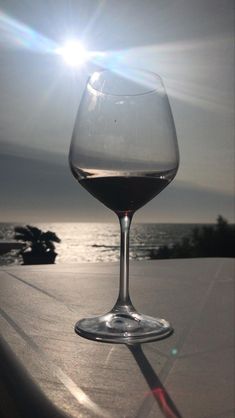 a glass of wine sitting on top of a table next to the ocean and sun