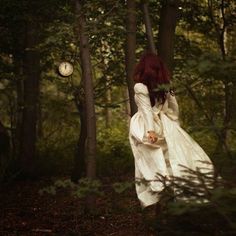 a woman in a white dress is walking through the woods with her back to the camera