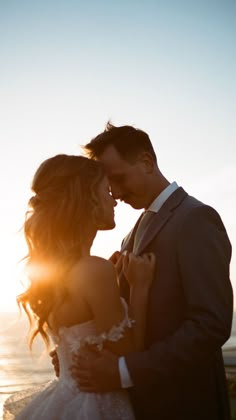 a bride and groom standing next to each other in front of the ocean at sunset