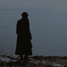 a woman standing on top of a hill next to the ocean looking out at the water