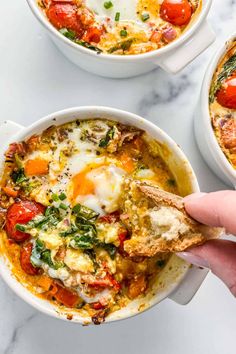 someone holding a piece of bread over a bowl of eggs and tomato soup with spinach