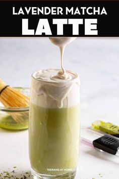 a glass filled with green liquid and topped with whipped cream next to other ingredients on a table