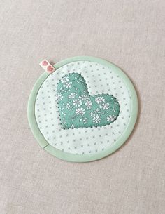 a green and white embroidered heart on a light gray background