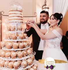 a bride and groom are cutting into a wedding cake with cupcakes on it