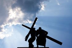 the silhouette of two people carrying a cross against a blue sky with clouds in the background