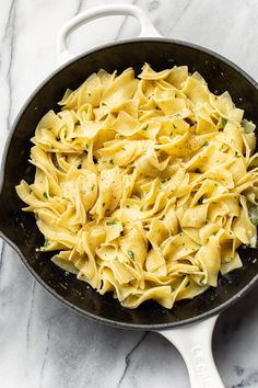 a skillet filled with pasta on top of a marble counter