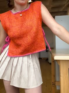 a woman in an orange sweater and white skirt