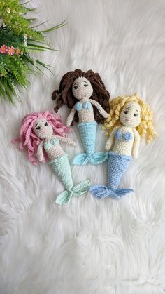 three crocheted mermaid dolls laying on a white furnishing next to a pine tree