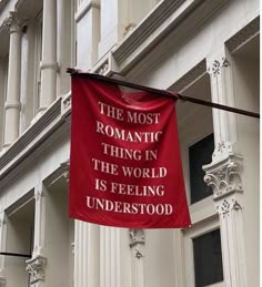 a red banner hanging from the side of a building that says, the most romantic thing in the world is feeling underfoot