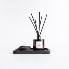 a candle and some candles on a tray with black sticks in front of white background