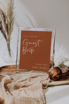 there is a sign that says guest book on the table next to some dried plants