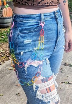 a woman in ripped jeans with colorful chains on her waist and leg, standing outside