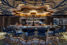 a bar with many chairs around it in a room that has an artistic ceiling design