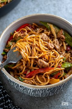 a close up of a bowl of noodles with meat and peppers on the side next to a fork