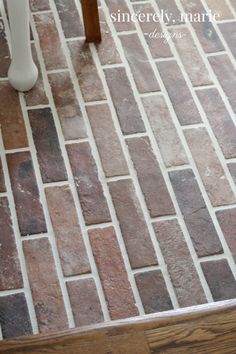 a white vase sitting on top of a wooden table next to a chair and tiled floor