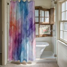 a bathroom with a shower curtain that has colorful watercolors on it, and a bathtub in the background