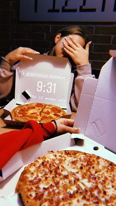 two people sitting at a table with pizzas in boxes and one person covering their eyes