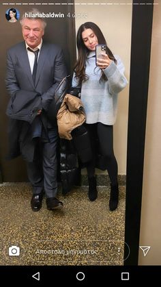 a man and woman standing next to each other in front of a mirror holding cell phones